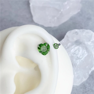 Detailed close-up of heart-shaped green zircon earring in silver prong setting on a model