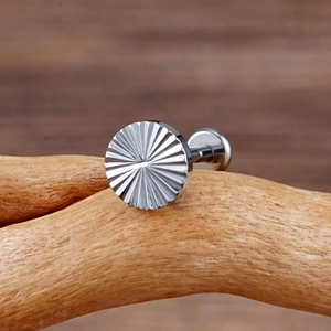 Macro detail of ASTM F136 titanium earring stud with sunburst texture on wood stand
