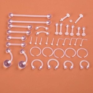 Macro detail of various clear acrylic body piercing jewelry set on orange background