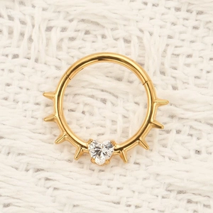 Close-up of golden titanium nose ring with spikes and heart-shaped CZ on white knit