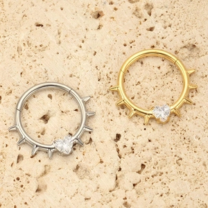 Detail of gold and silver heart CZ hinged rings with punk spikes on a stone surface