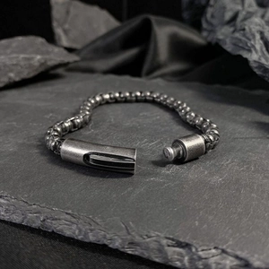 Détail d'un bracelet gourmette en acier industriel avec finition mate sur texture de roche