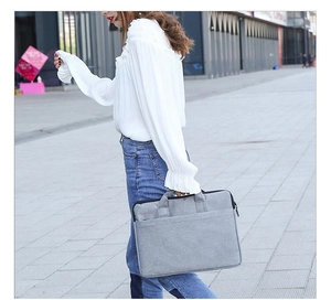 Graue Laptoptasche aus Stoff mit Tragegriff und Fronttasche in einer Outdoor-Straßenszene