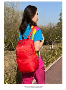 Red waterproof outdoor backpack with adjustable straps shown in an outdoor park setting