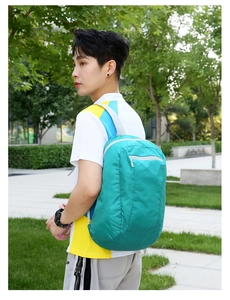 Outdoor foldable backpack in bright cyan waterproof nylon shown in a park setting