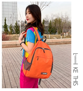 Outdoor view of a lightweight orange foldable backpack with side mesh pocket and zip closure