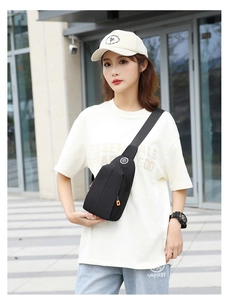 Detailed street style view of a black oxford chest bag with orange zipper puller and strap