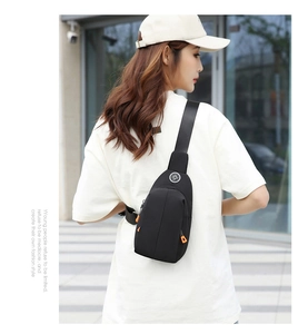 Outdoor shot of a black waterproof oxford sling bag with vibrant orange zipper pull tabs