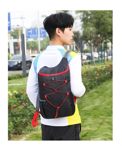 Outdoor foldable travel backpack in black with red accents worn by a model in a park