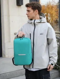 Close-up of mint green backpack with reflective strip held by handle in outdoor setting