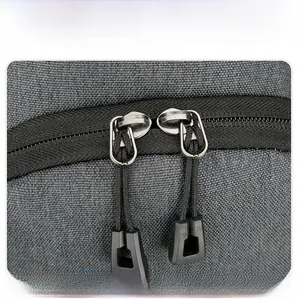 Close-up of grey fabric chest bag showing durable metal dual zippers with pull tabs