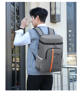 Gray insulated picnic backpack with orange straps worn by a man in an outdoor setting
