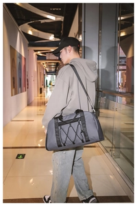 Modelo masculino lleva bolsa de viaje gris grande en centro comercial, ideal para el deporte