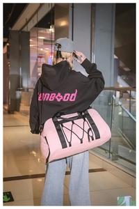 Bolso de viaje rosa con correas negras y cordón elástico usado por una modelo
