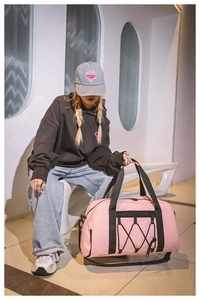 Bolsa de viaje rosa con asas negras mostrada por una modelo en un entorno moderno