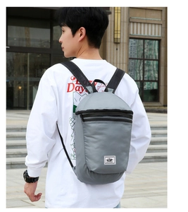 Side view of the lightweight grey foldable backpack worn by a model in an outdoor setting