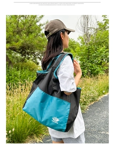 Outdoor view of a model carrying a large blue and black travel tote bag with Vanaheimr logo