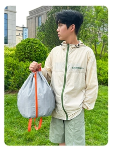 Gray foldable sports backpack with orange zippers shown in an outdoor travel setting