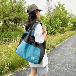 Large capacity black folding travel tote bag with turquoise edges shown in outdoor setting