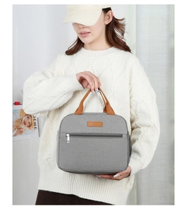 Detailed view of grey Oxford cloth lunch bag with brown leather handles and side mesh pocket