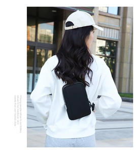 Outdoor urban view of a black waterproof crossbody sling bag with adjustable buckle strap