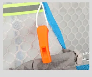 Detail of outdoor backpack featuring an orange survival whistle buckle and reflective strip