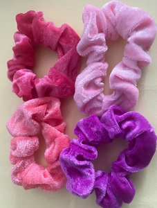 Detail view of four velvet scrunchies in shades of pink and purple with soft texture