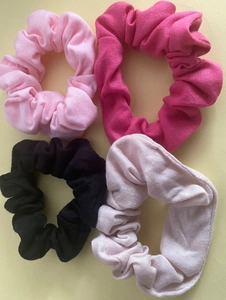 Close-up of four colorful elastic satin scrunchies in pink, rose, black, and light pink
