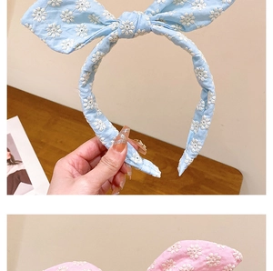 Détail de la broderie de fleurs blanches sur les serre-têtes oreilles de lapin rose et bleu