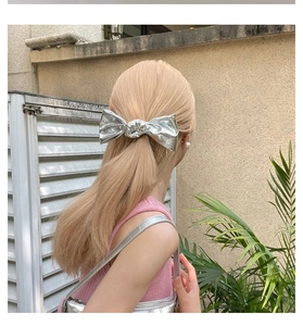 Detail view of a metallic silver bow hair clip worn by a model in outdoor setting