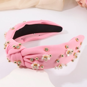 Détail du serre-tête noué rose avec fleurs blanches, strass et perles sur fond de satin