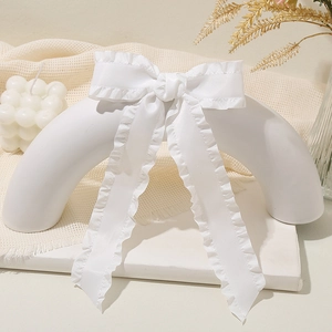 Elegant white satin bow hair clip with ruffled edges and long ribbons in a stylish setup