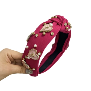 Deep rose red fabric headband with pearls, crystals and enamel hearts on white background