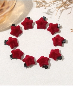 Close-up of ten red velvet star hair clips arranged in a circle on a textured beige surface