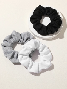 Three knit scrunchies in black, gray, and white on a stone base showing ribbed texture