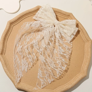 Elegant white lace bow hair clip with embroidered mesh ribbons on a ceramic tray