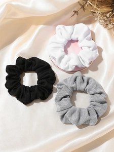 Three-piece set of textured knit scrunchies in black, white, and grey on a marble plate