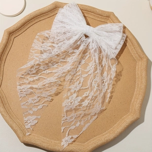 Elegant white lace bow hair clip with floral patterns and long ribbons on a tray