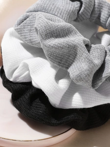 Close-up of ribbed knit scrunchies in black, white, and grey on a ceramic plate