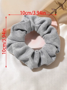 Macro shot of a 10cm grey knitted scrunchie showing fine fabric texture on a soft tray