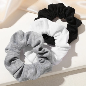 Three-pack ribbed knit hair scrunchies in grey, white, and black on a stone display