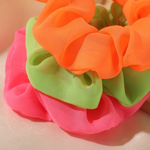 Nahaufnahme von drei leuchtenden Mesh-Haargummis in Orange Grün und Pink Farben