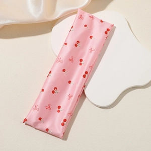 Pink satin headband detail with printed red cherries and tiny bows on silk texture