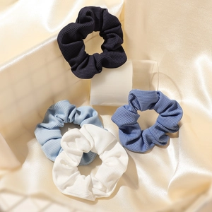 Set of four textured scrunchies in black and blue shades on champagne silk background