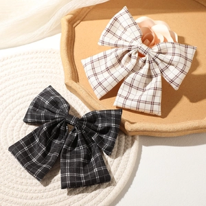 Vintage checkered bow hair clips in black and cream beige, set on a woven tray