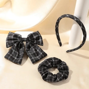 Detailed set of black and white plaid hair clip, headband, and scrunchie on silk backdrop