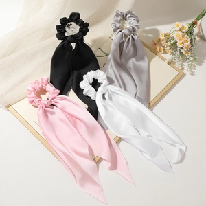 Detail of four satin ribbon hair scrunchies in black grey pink and white on silk fabric