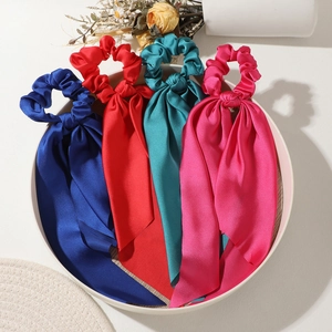 Close-up of four colorful satin bow hair ties with long ribbons in vibrant silk texture