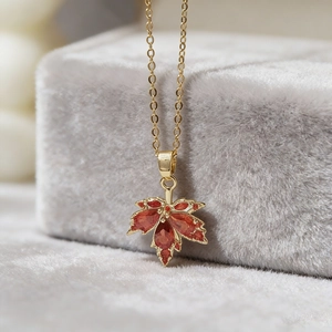 Golden maple leaf pendant necklace with red crystals on a gray velvet jewelry box