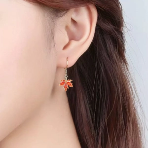 Close-up of maple leaf rhinestone drop earrings with warm orange stones on model